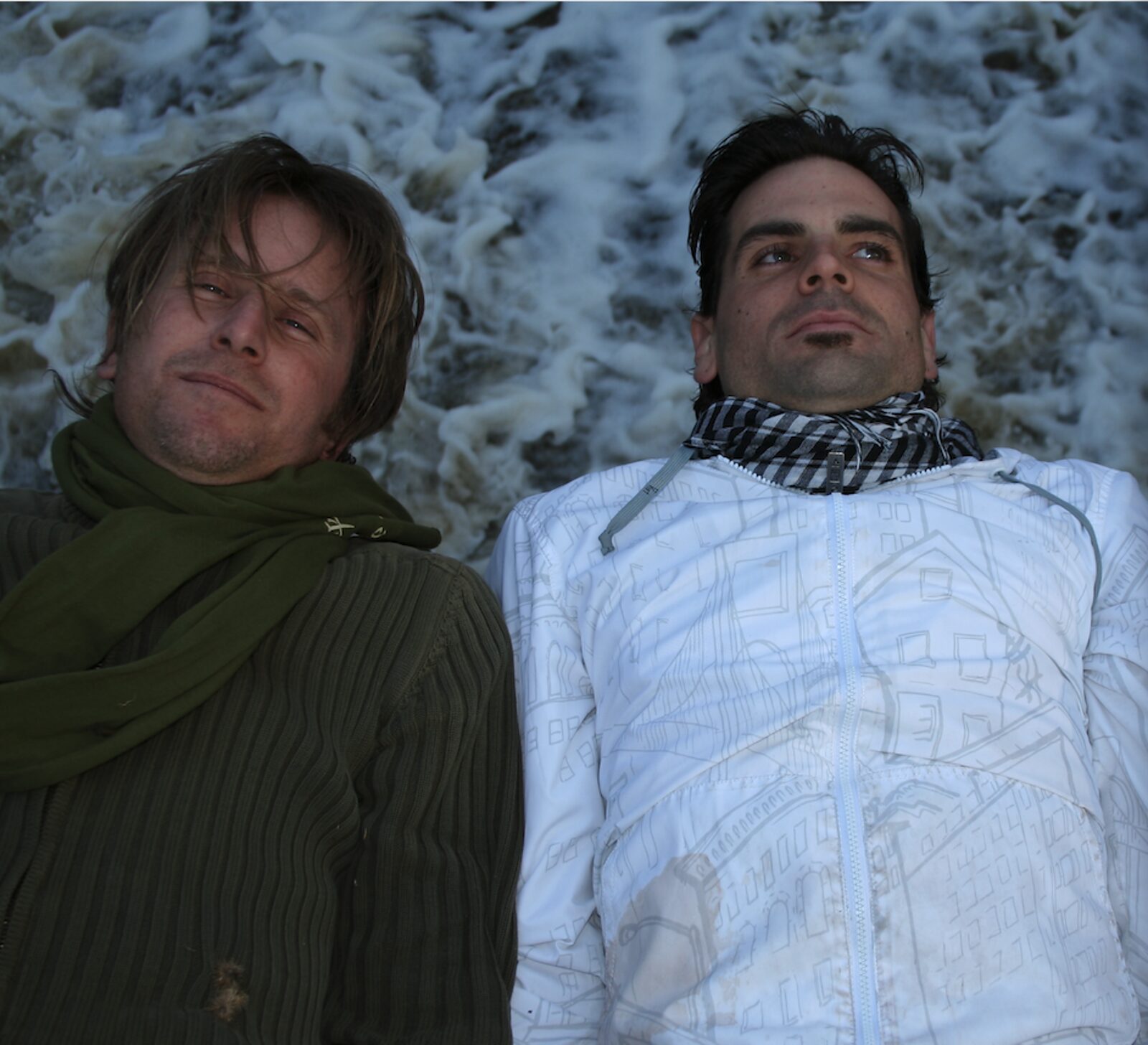 Two band members lying side by side against churning white river foam