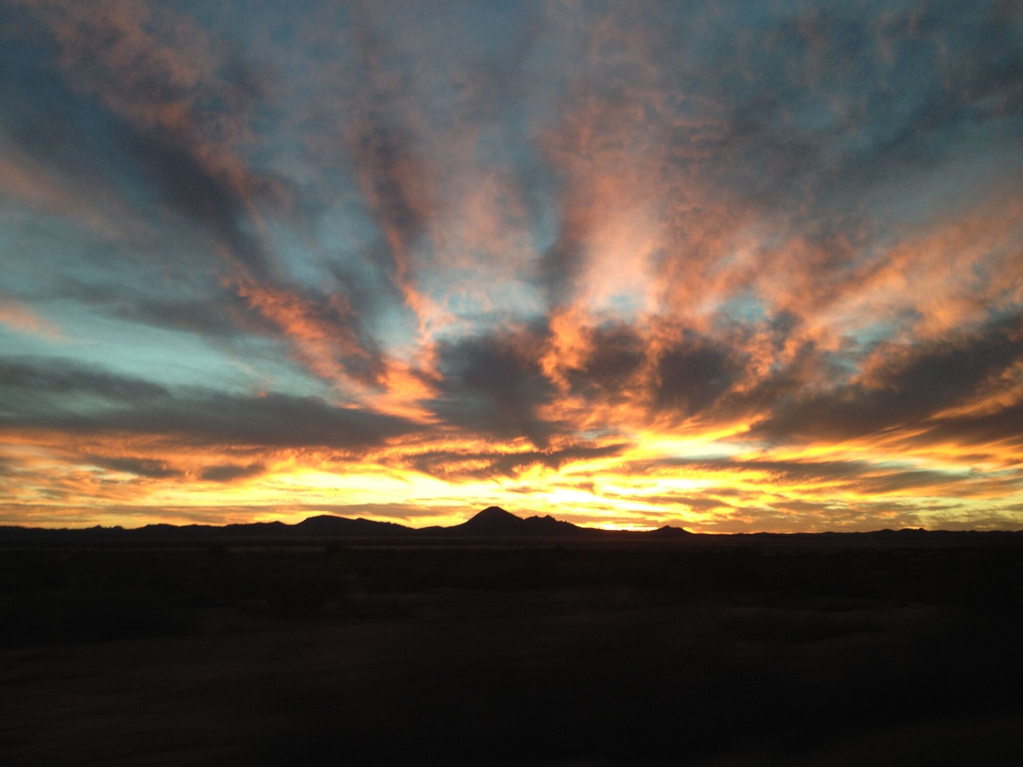 Desert sunset: fire-orange clouds fanning over silhouetted mountains